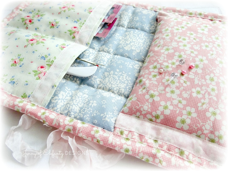 May include: A quilted fabric storage pouch with three pockets and a padded section. The pouch is decorated with floral patterns in pink, blue, and white.