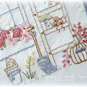 Könnte beinhalten: Nahaufnahme eines weißen Stoffes mit gestickten Details, darunter ein kleines Haus mit einem Fenster, eine Leiter, ein Kürbis und Blumen. Der Stoff ist mit braunem, blauem und rosa Garn gestickt.