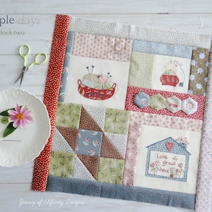 May include: A patchwork quilt block in a red, white and blue colour scheme. The block features a variety of patterns, including floral, geometric and polka dots. The block also includes three embroidered images: a bowl of yarn, a sewing box and a house with the text "Love grows here".