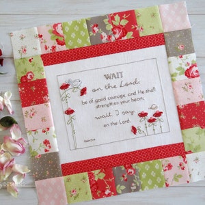 May include: A square, quilted wall hanging with a floral design and the text "WAIT on the Lord." The border is made of red, pink, and green floral fabric squares. Embroidered flowers and a bird accent the text.