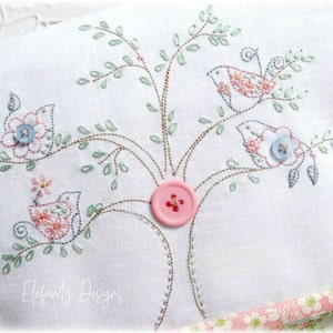 May include: Embroidered white fabric with a tree design featuring three birds, pink and blue flowers, and a pink button. The text "Elfauts Designs" is embroidered at the bottom.