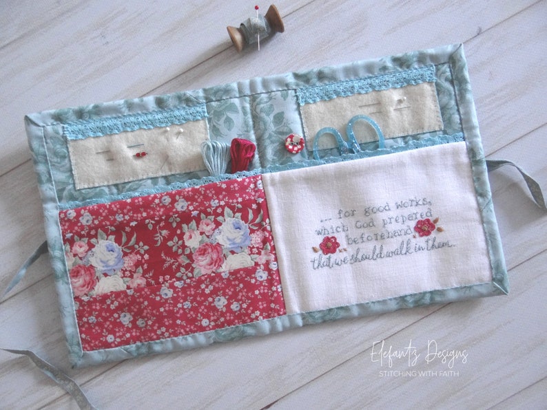May include: A blue and red fabric sewing roll-up with multiple pockets and compartments. The roll-up has a white fabric panel with the embroidered text "...for good works, which God prepared beforehand that we should walk in them." The roll-up is labeled "Elefants Designs STITCHING WITH FAITH".