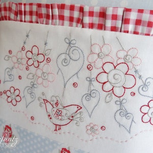 May include: A white pillow with a red and white gingham trim and embroidered design. The design features a bird, hearts, and flowers in shades of red, pink, and grey.