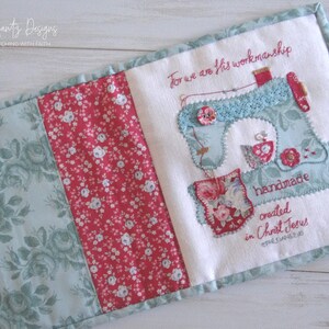 May include: A white fabric book with a blue and white sewing machine design and the text "For we are His workmanship handmade created in Christ Jesus Ephesians 2:10". The book is decorated with floral fabric in shades of pink, red, and green.