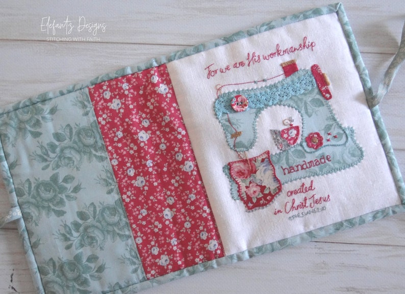 May include: A white fabric book with a blue and white sewing machine design and the text "For we are His workmanship handmade created in Christ Jesus Ephesians 2:10". The book is decorated with floral fabric in shades of pink, red, and green.
