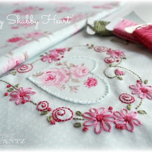 Puede incluir: Una tela azul claro con bordado floral rosa en forma de corazón. El texto "My Shabby Heart" está bordado en la esquina superior izquierda de la tela.