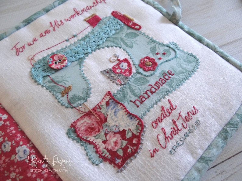 May include: A white fabric book with a blue and green sewing machine design. The book has red and white floral fabric accents and the text "For we are His workmanship" and "handmade created in Christ Jesus Ephesians 2:10".