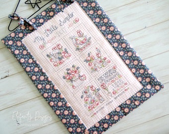 May include: A pink and white gingham fabric sampler with embroidered designs, including a bird, flowers, and the alphabet. The sampler is framed with a blue and pink floral fabric border and has the text "My Little Sampler 2017" at the top.