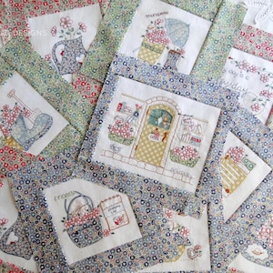 Peut inclure: Une courtepointe patchwork avec des broderies florales et des motifs de jardin. Les carrés de la courtepointe présentent des images d'arrosoirs, de paniers de fleurs et de portes, avec le mot "Thursday" visible. La courtepointe est encadrée de tissu à motifs floraux.