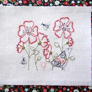 Pode incluir: Design floral bordado em tecido branco. Apresenta flores delineadas em vermelho, caules verdes e um pássaro com detalhes florais. Inclui abelhas bordadas e um coração. O fundo é um padrão floral.