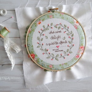 Puede incluir: Un aro de bordado verde y blanco con un dise&ntilde;o floral y la cita "Qu&eacute; dulce deleite ofrece una vida tranquila - William Drummond" bordada en hilo rosa.