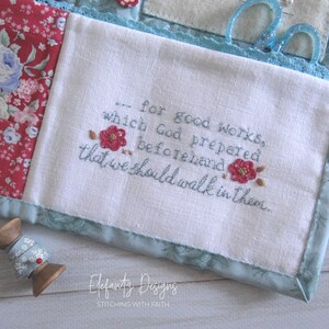 May include: A white fabric pouch with a blue border and a quote embroidered in blue thread: "...for good works, which God prepared beforehand that we should walk in them." The pouch is decorated with a floral pattern and has a small wooden spool of thread next to it.