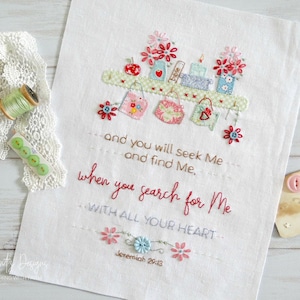 Puede incluir: Tela blanca bordada con una cita de Jerem&iacute;as 29:13, "Y me buscar&eacute;is y me hallar&eacute;is, cuando me busqu&eacute;is de todo vuestro coraz&oacute;n." El bordado presenta un estante con peque&ntilde;os frascos, libros y flores.