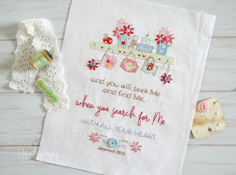 Puede incluir: Tela blanca bordada con una cita de Jerem&iacute;as 29:13, "Y me buscar&eacute;is y me hallar&eacute;is, cuando me busqu&eacute;is de todo vuestro coraz&oacute;n." El bordado presenta un estante con peque&ntilde;os frascos, libros y flores.