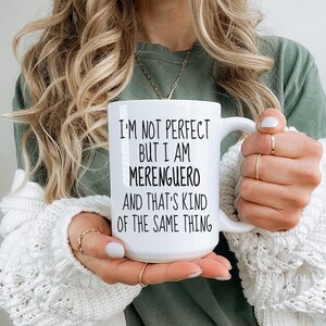 Peut inclure: Une tasse à café en céramique blanche avec du texte noir qui dit "Je ne suis pas parfait mais je suis Merenguero et c'est un peu la même chose."