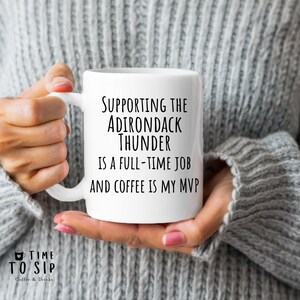 May include: White ceramic coffee mug with black text that reads "Supporting the Adirondack Thunder is a full-time job and coffee is my MVP".