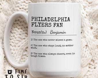 Pode incluir: Caneca de café de cerâmica branca com um design preto que diz "Philadelphia Flyers Fan" e define o termo como "Aquele que nunca perde um jogo. Aquele que permanece alto, não importa o que aconteça. Aquele que sempre torce, mesmo em tempos difíceis."