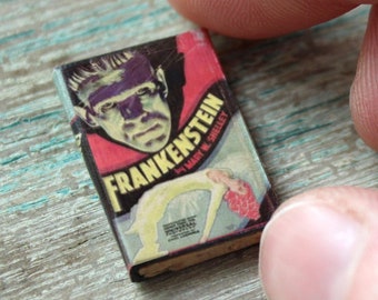 Könnte beinhalten: Ein Miniatur-Taschenbuch mit einem roten, weißen und schwarzen Umschlag, der eine Schwarzweißillustration eines Monsters mit dem Titel "Frankenstein" von Mary W. Shelley zeigt.