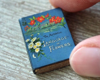 May include: A small blue book with the title "The Artistic Language of Flowers" on the cover. The cover features red and white flowers.