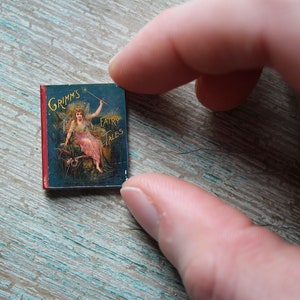 May include: A small, red-bound book with a blue cover featuring an illustration of a woman in a white dress holding a wand. The book's title is "Grimm's Fairy Tales".