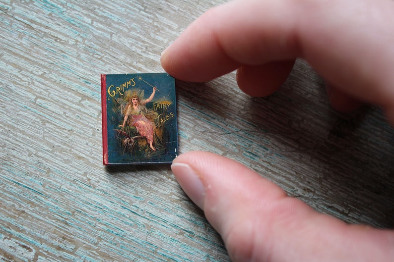 May include: A small, red-bound book with a blue cover featuring an illustration of a woman in a white dress holding a wand. The book's title is "Grimm's Fairy Tales".