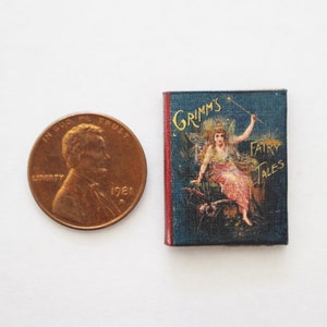May include: A miniature book with a blue cover and gold lettering. The cover features an illustration of a fairy with a wand, sitting on a cloud. The title of the book is "Grimm's Fairy Tales".