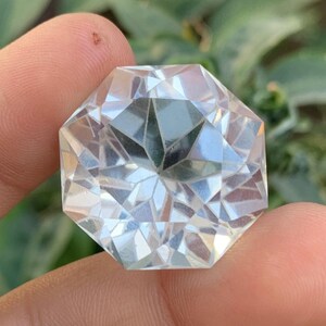 Puede incluir: Un cristal transparente, facetado, octogonal con un patrón en forma de estrella en su interior. El cristal se sostiene en una mano.