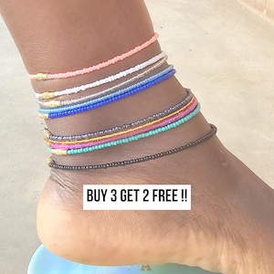 May include: Ankle bracelets in various colors, including pink, white, blue, and brown. The bracelets are made of small beads and are stacked on the ankle. The text "BUY 3 GET 2 FREE !!" is displayed.