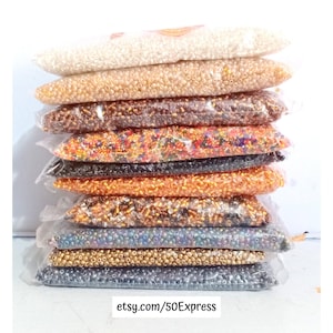 May include: A stack of clear plastic bags filled with small, colorful beads. The beads are in various colors, including white, gold, brown, orange, and black. The text "etsy.com/50Express" is visible at the bottom of the image.