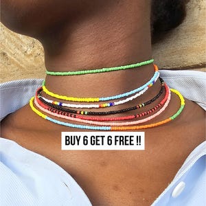 May include: A collection of colorful beaded choker necklaces in various shades, including green, yellow, blue, and orange. The necklaces are layered and worn around the neck. The image includes the text "BUY 6 GET 6 FREE !!".