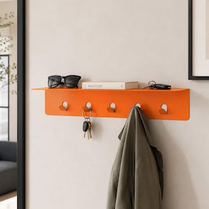 May include: A bright orange wall-mounted shelf featuring five integrated hooks. The shelf holds a pair of black sunglasses and a book titled Matisse. A set of keys hangs from one hook, and a gray jacket hangs from another hook on the metal rack.