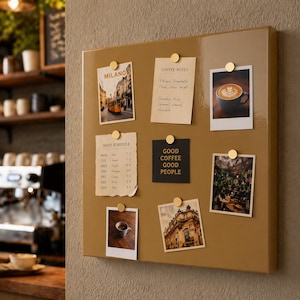 May include: A rectangular, tan-colored magnetic board with several polaroid-style photos and notes attached with gold-colored magnets. The photos depict coffee, cityscapes, and cafe scenes. Text on the board includes "MILANO", "COFFEE NOTES", and "GOOD COFFEE GOOD PEOPLE".