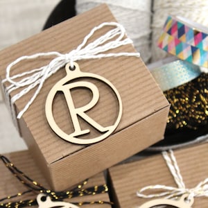 May include: Three small brown gift boxes with white string bows and wooden circle ornaments with the letters R, T, and S.