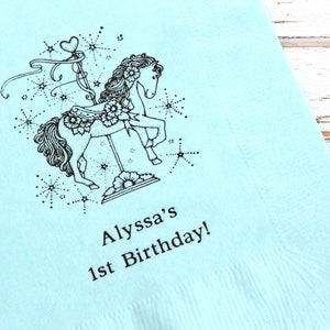 May include: A light blue paper napkin with a black and white illustration of a carousel horse with stars and the text "Alyssa's 1st Birthday!"