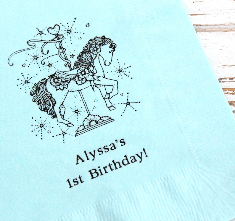 May include: A light blue paper napkin with a black and white illustration of a carousel horse with stars and the text "Alyssa's 1st Birthday!"