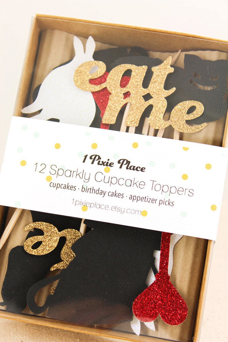 May include: A set of 12 sparkly cupcake toppers featuring a white rabbit, a red heart, a black cat, and the words "eat me" in gold glitter. The toppers are packaged in a clear plastic box with a white label that reads "1 Pixie Place 12 Sparkly Cupcake Toppers cupcakes birthday cakes appetizer picks 1pixieplace.etsy.com".