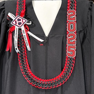May include: A black and red graduation lei with the text "2025" in red and white. The lei is braided with black and red ribbons. A white ribbon with the text "Congratulations Rhiannon!" and "CBHS Class of 2025" is attached.