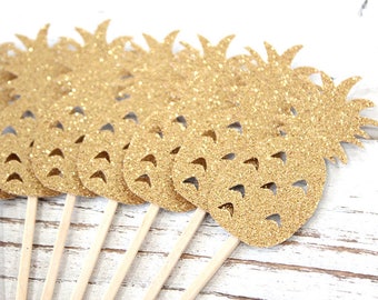 May include: A collection of gold glitter pineapple-shaped party decorations on wooden sticks. The pineapples have cut-out details and are arranged in a row, perfect for tropical-themed events or celebrations.