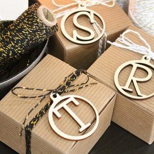 May include: Three small gift boxes wrapped in brown paper with black and gold string. Each box has a wooden circle ornament with a letter, S, R, and T, attached.