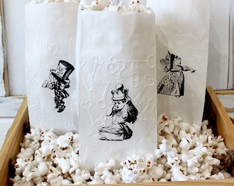 May include: Three white paper bags filled with popcorn, each featuring a different black and white illustration from Alice in Wonderland. The illustrations include the Mad Hatter, the Queen of Hearts, and Alice.