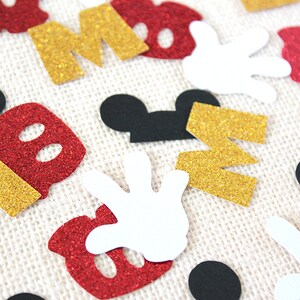 May include: Assortment of red, gold, black and white confetti featuring Mickey Mouse ears, gloves, and the letters "M" and "O".