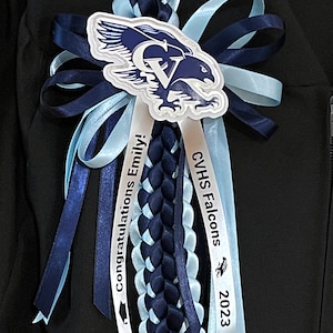 May include: A graduation lei in navy blue and light blue, featuring a braided design and ribbons. The lei includes a school logo with an eagle and the text "CVHS Falcons 2023". Ribbons say "Congratulations Emily!"