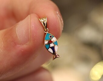 May include: A gold fish charm with blue, white, and red enamel detailing. The charm is held by a finger.