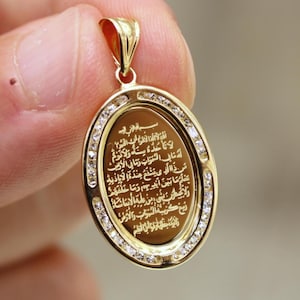 May include: A gold oval pendant with a decorative border of small clear stones. The pendant features an inscription in Arabic script.