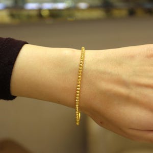 Puede incluir: Un brazalete de oro con un dise&ntilde;o de cuentas. El brazalete est&aacute; en la mu&ntilde;eca de una persona.