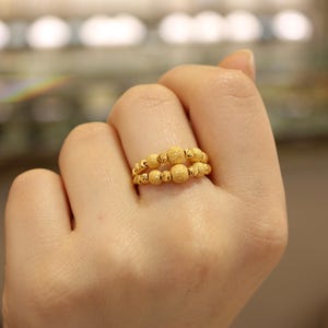 May include: A gold ring with a textured design. The ring is made up of multiple small, round beads.