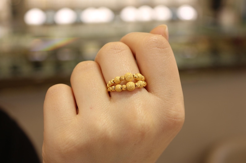 May include: A gold ring with a textured design. The ring is made up of multiple small, round beads.