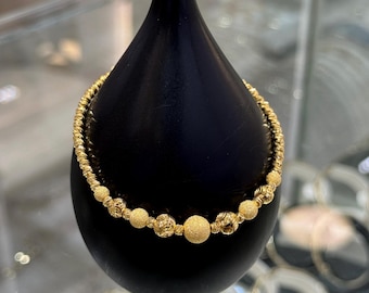 Può includere: Un braccialetto d'oro con una catena intrecciata strutturata e perline rotonde alternate. Le perline hanno una finitura opaca e sono di dimensioni variabili. Il braccialetto è esposto su un supporto nero a forma di goccia.