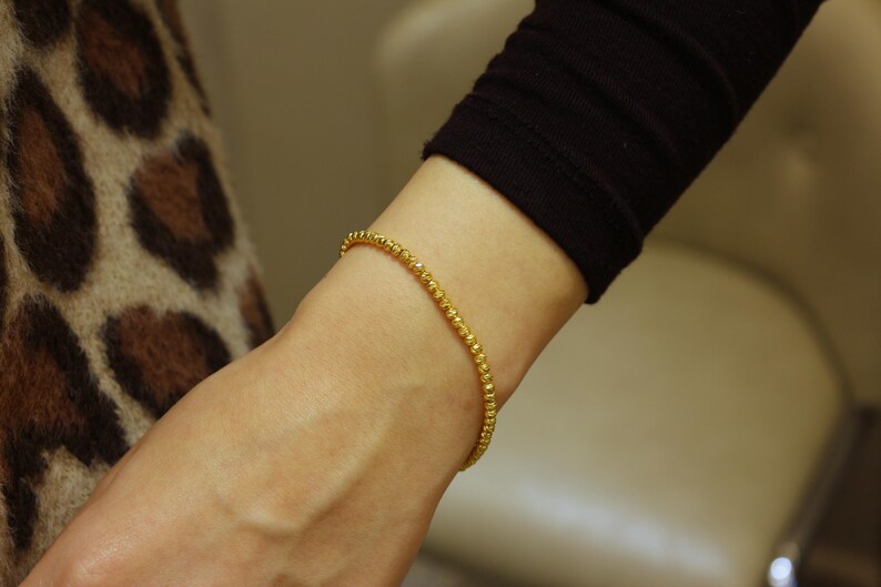 Puede incluir: Un brazalete de cuentas doradas en la mu&ntilde;eca.