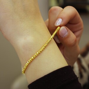 Puede incluir: Un brazalete de oro con un dise&ntilde;o de cuentas. El brazalete est&aacute; en la mu&ntilde;eca de una persona.